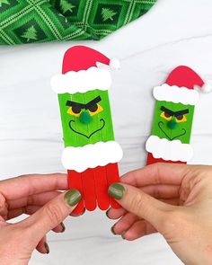 two hands holding up small pieces of paper with the faces of characters in santa hats