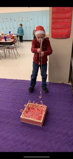 a young boy standing on top of a purple carpet next to a box filled with yarn