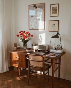 a wooden desk topped with a laptop computer next to a vase filled with red flowers