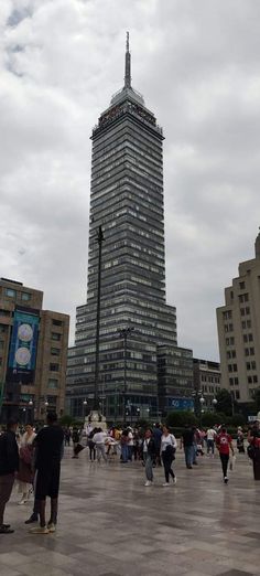 many people are walking around in front of tall buildings and skyscrapers on a cloudy day