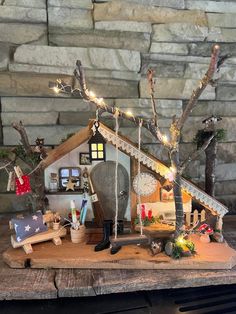 a wooden table topped with a miniature house covered in christmas lights and decorations next to a stone wall