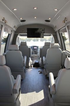 the inside of a vehicle with several seats and television in the back area, facing forward