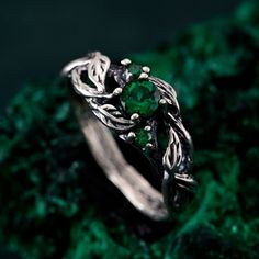 a green ring sitting on top of a mossy rock with leaves and vines around it