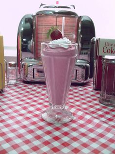 a pink smoothie in a tall glass on a checkered tablecloth with toasters