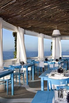 an outdoor restaurant with blue tables and white chairs overlooking the ocean on a sunny day