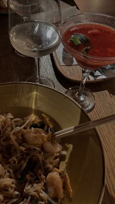 a bowl filled with noodles and shrimp next to a glass of red wine on a table