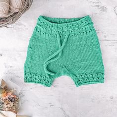 a green knitted shorts sitting on top of a white table next to a ball of yarn