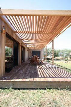 a wooden deck with chairs and tables under a pergolated roof over an open field