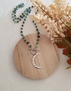 This bohemian style necklace features a dainty beaded Emerald chain that consists of tiny natural Emeralds wire wrapped together. A popular silver toggle clasp in the front is accented with a beautiful hammered design crescent Moon pendant. Your choice of length. Emerald: A stone of divine love, luck, intelligence and peace. Emerald green is the color that is used to align the heart chakra, allowing love to flow freely from a person's core. Helps eliminate negative energy and restore confidence Bohemian Necklaces With Moon Charm And Round Beads, Bohemian Beaded Necklaces With Moon Charm, Bohemian Beaded Necklace With Moon Charm, Bohemian Moon Phase Round Beaded Jewelry, Adjustable Bohemian Beaded Necklace With Moon Charm, Bohemian Moon-shaped Necklaces With Natural Stones, Bohemian Moon Shaped Necklace With Natural Stones, Bohemian Moon-shaped Necklace With Natural Stones, Handmade Bohemian Toggle Necklace As Gift