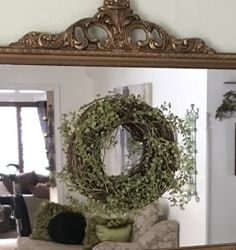 a mirror reflecting a living room with a wreath on the wall and a couch in front of it