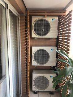 two air conditioners sitting next to each other near a window with shutters on it