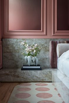 a bedroom with pink walls and white bedding, flowers in vases on the nightstand