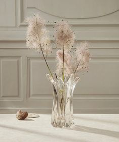 a glass vase filled with pink flowers on top of a white table next to shells