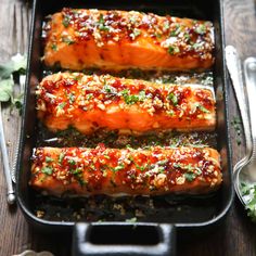 three salmon fillets in a pan with seasoning on top and spoons to the side