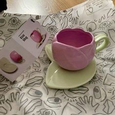 a pink cup and saucer sitting on top of a table next to a card