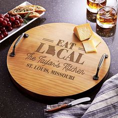 a wooden cutting board with the words eat local on it next to two glasses of wine and cheese