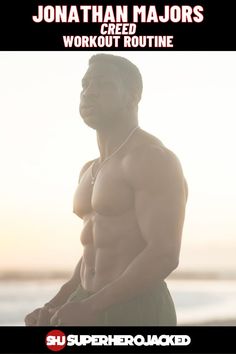 a man with no shirt on standing in front of the ocean and holding his hands behind his back