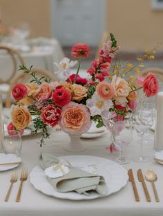 an arrangement of flowers in a vase on top of a table with place settings and napkins