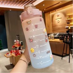 a person holding up a water bottle with stickers on it in front of a counter