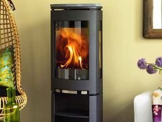 a wood burning stove in a living room with wicker chair and vase on the floor