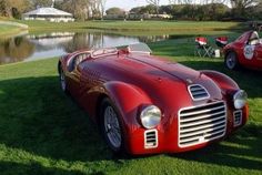 two red sports cars parked next to each other in the grass near a body of water