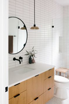 a white tiled bathroom with wooden cabinets and a round mirror above the sink, along with a potted plant