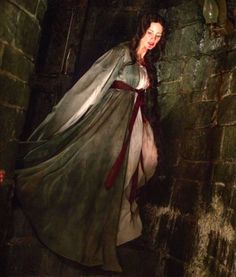 a woman dressed in medieval clothing is walking through a dark tunnel with her hands on her hips