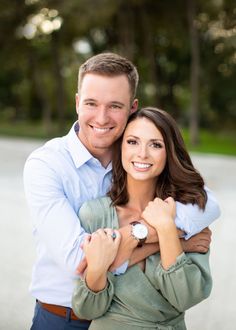 a man and woman hugging each other in front of the camera with trees in the background