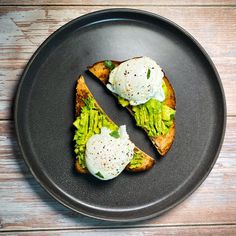 two pieces of toast with avocado and poached eggs on them sitting on a black plate