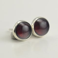 This pair of all sterling silver stud earrings features 7mm garnets. The sterling silver settings have been polished for a bright, shiny finish. These earrings are backed with sterling silver heavy-weight ear nuts. The earring posts are 3/8" in length. The earrings pictured are the ones you will receive Please read my shipping and policies page on the tab above or at this link: https://www.etsy.com/shop/laurenmeredith/policy?ref=shopinfo_policies_leftna All orders come packaged in a gift box with a bow, ready for giving. Silver Garnet Birthstone Earrings, Classic Silver Garnet Earrings, Classic Round Garnet Earrings, Sterling Silver Studs, Sterling Silver Earrings Studs, Silver Studs, Silver Earrings Studs, Jewelry Earrings Studs, Post Earrings