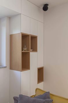 a room with white walls and wooden shelves on the wall next to a yellow couch