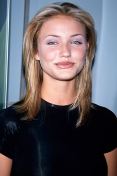 a woman with blonde hair and blue eyes smiles at the camera while standing in front of a poster