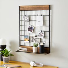 a wooden desk with a metal grid on the wall and various office supplies sitting on it