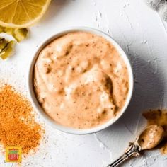 a white bowl filled with sauce next to sliced oranges and spices on a table