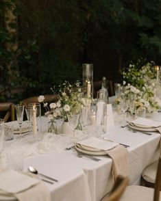 the table is set with white flowers, candles and place settings for an elegant dinner