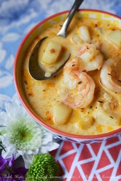 a bowl of soup with shrimp and dumplings in it on a table next to flowers