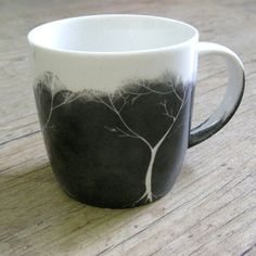 a black and white coffee cup sitting on top of a wooden table with trees painted on it