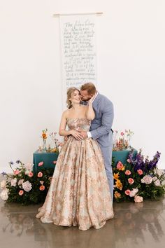 a man and woman standing next to each other in front of a wall with flowers