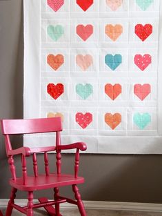 a red rocking chair sitting next to a wall hanging with heart shaped squares on it