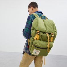 a man wearing a green backpack and tan pants is looking down at his back pocket