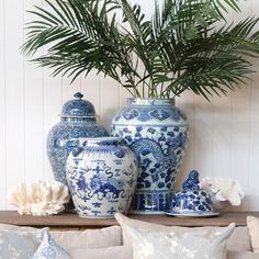 three blue and white vases sitting on top of a table next to a plant