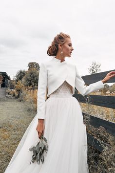 a woman in a wedding dress leaning against a fence with her hand on the rail