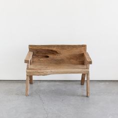 a wooden bench sitting on top of a cement floor in front of a white wall