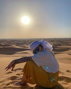 a person sitting in the sand wearing sunglasses and a white hat