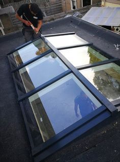 a man standing on top of a roof next to an upside down glass window with multiple panes