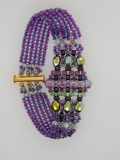 Luxurious Art Deco Bracelet is made with several types and sizes of beads in purples and greens. Closure is a 3-strand slide clasp in gold finish. Other color combos are available here on my Etsy site. Design by Smadar Grossman of Smadar's Treasure. Created by Tara of Takeen Arts. Item B1276. Purple Bracelets With Polished Beads For Jewelry Making, Purple Polished Beads Bracelet For Jewelry Making, Purple Polished Beads Bracelets For Jewelry Making, Handmade Purple Multi-strand Bracelets, Handmade Purple Multi-strand Bracelet, Handmade Purple Multi-strand Beads, Purple Multi-strand Beads For Jewelry Making, Purple Beaded Oval Jewelry, Adjustable Purple Double Strand Jewelry