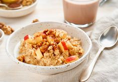 a bowl of oatmeal with apples and walnuts next to a glass of milk