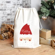 a white bag with a santa clause on it sitting next to presents and a christmas tree