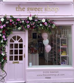 a pink store front with flowers and balloons in the window display area, along with an arched doorway