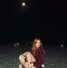 a woman is sitting on a chair in the water at night with her legs crossed